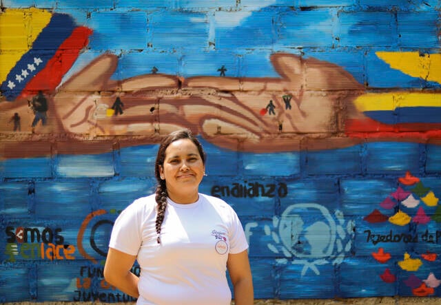 Omaira faces the camera, stood against a colorful painted wall.